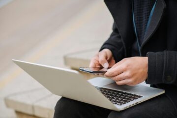 Crop anonymous male worker with netbook touching screen of cellphone while working on street staircase