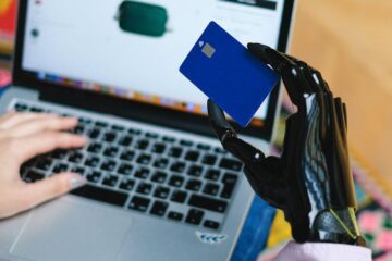 Person with prosthetic hand using laptop for online shopping, holding a credit card.